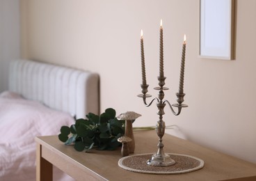 Photo of Stylish candlestick with burning candles and other decor on wooden table near beige wall indoors