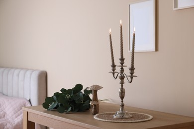 Photo of Stylish candlestick with burning candles and other decor on wooden table near beige wall indoors
