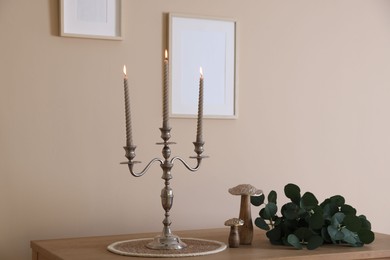 Photo of Stylish candlestick with burning candles and other decor on wooden table near beige wall indoors