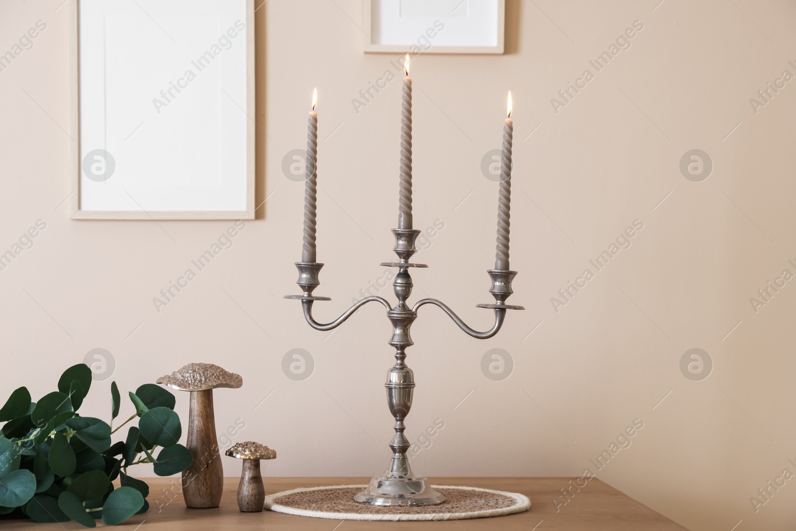 Stylish candlestick with burning candles and other decor on wooden table near beige wall indoors Photo of Stylish candlestick with burning candles and other decor on wooden table near beige wall indoors