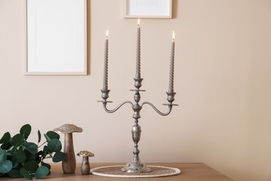 Photo of Stylish candlestick with burning candles and other decor on wooden table near beige wall indoors