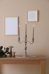 Photo of Stylish candlestick with burning candles and other decor on wooden table near beige wall indoors