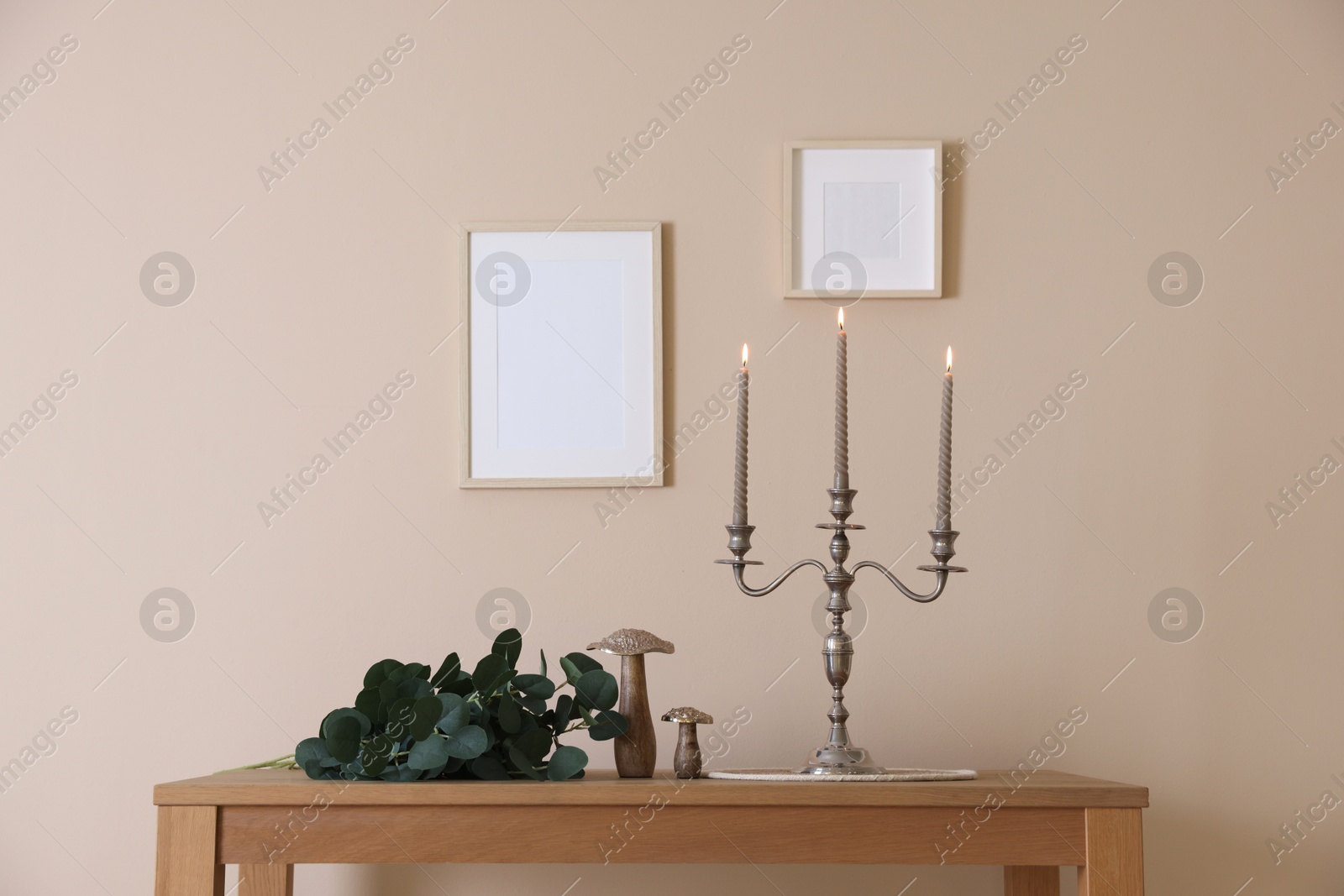 Stylish candlestick with burning candles and other decor on wooden table near beige wall indoors Photo of Stylish candlestick with burning candles and other decor on wooden table near beige wall indoors