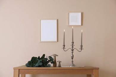Photo of Stylish candlestick with burning candles and other decor on wooden table near beige wall indoors