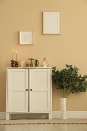 Photo of Stylish candlesticks with burning candles and other decor on cabinet near beige wall indoors