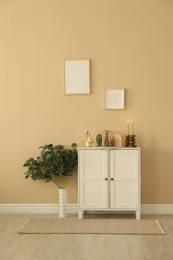 Photo of Stylish candlesticks with burning candles and other decor on cabinet near beige wall indoors
