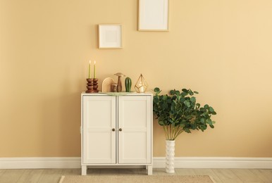 Photo of Stylish candlesticks with burning candles and other decor on cabinet near beige wall indoors