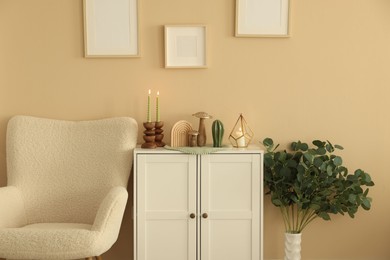 Photo of Stylish candlesticks with burning candles and other decor on cabinet near beige wall indoors