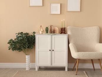 Photo of Stylish candlesticks with burning candles and other decor on cabinet near beige wall indoors