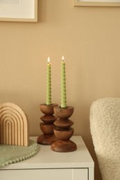 Photo of Stylish candlesticks with burning candles and other decor on cabinet near beige wall indoors