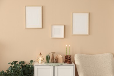 Photo of Stylish candlesticks with burning candles and other decor on cabinet near beige wall indoors