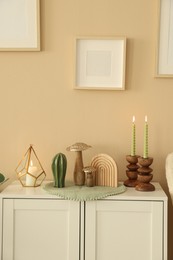 Photo of Stylish candlesticks with burning candles and other decor on cabinet near beige wall indoors