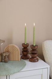 Photo of Stylish candlesticks with burning candles and other decor on cabinet near beige wall indoors