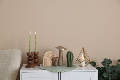 Photo of Stylish candlesticks with burning candles and other decor on cabinet near beige wall indoors