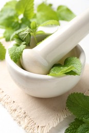 Photo of Fresh lemon balm leaves and pestle in mortar on white table, closeup