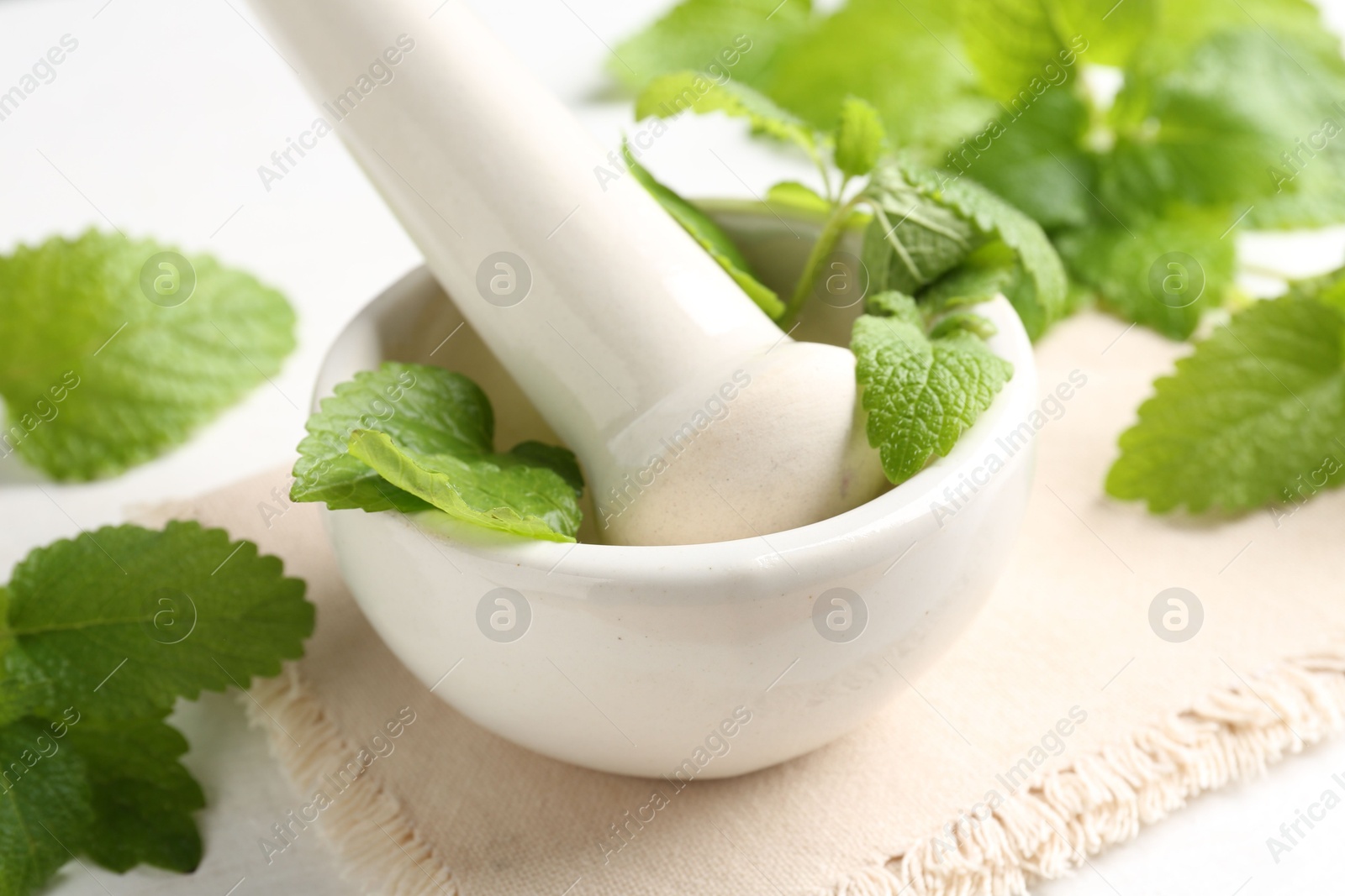 Fresh lemon balm leaves and pestle in mortar on white wooden table, closeup Photo of Fresh lemon balm leaves and pestle in mortar on white wooden table, closeup