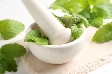 Photo of Fresh lemon balm leaves and pestle in mortar on white wooden table, closeup