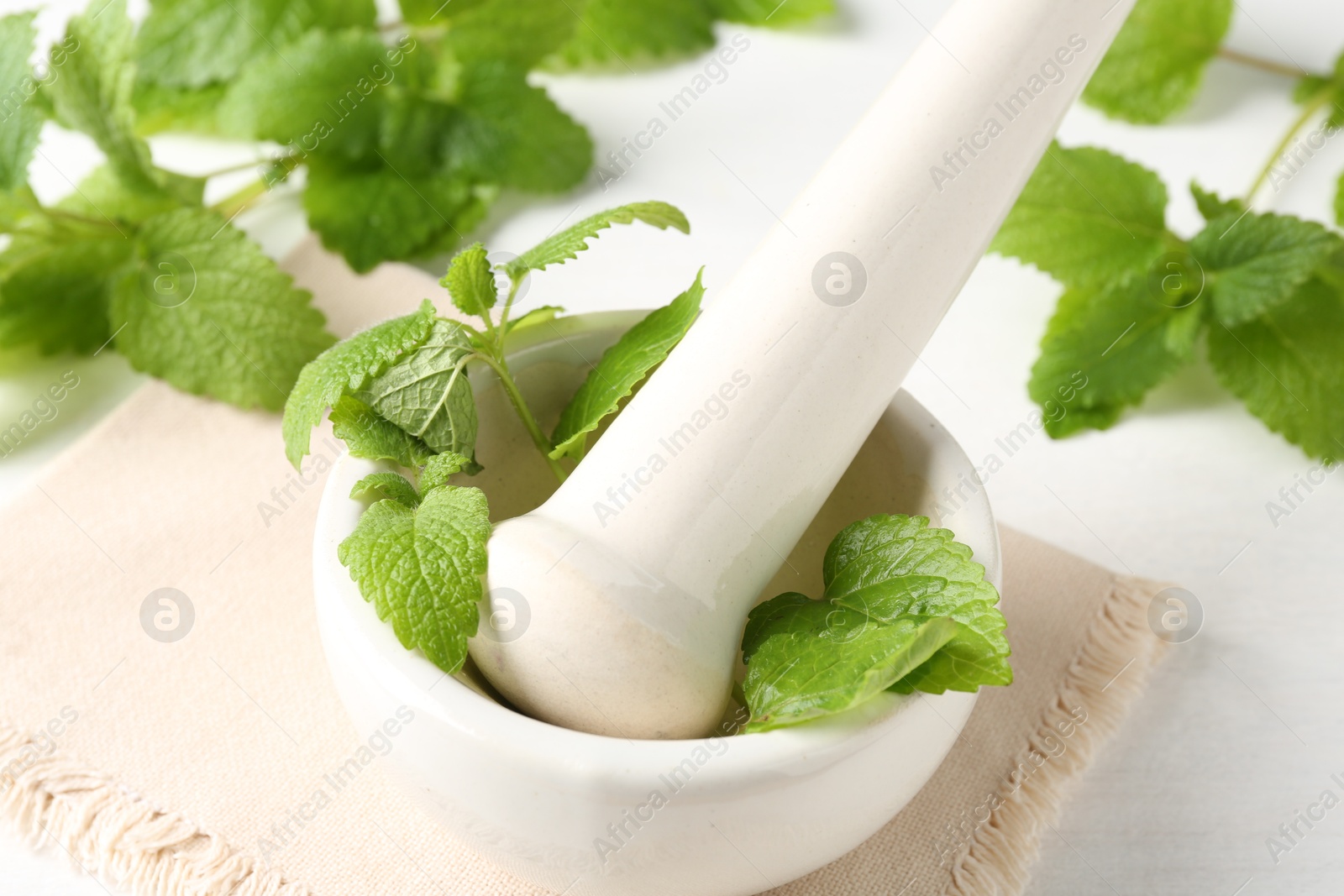 Fresh lemon balm leaves and pestle in mortar on white wooden table, closeup Photo of Fresh lemon balm leaves and pestle in mortar on white wooden table, closeup