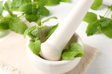 Photo of Fresh lemon balm leaves and pestle in mortar on white wooden table, closeup