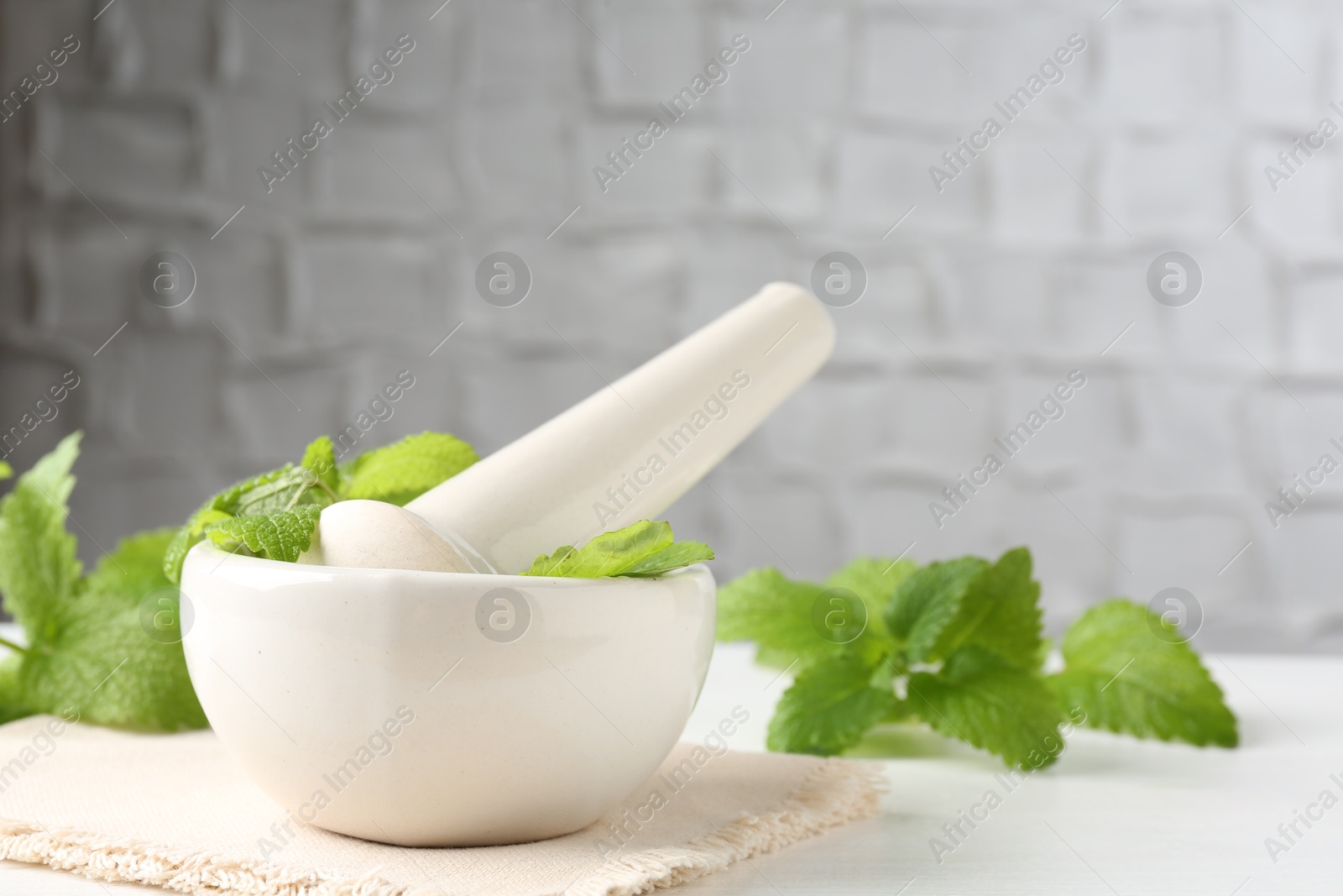 Fresh lemon balm leaves and pestle in mortar on white wooden table Photo of Fresh lemon balm leaves and pestle in mortar on white wooden table