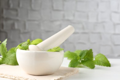 Photo of Fresh lemon balm leaves and pestle in mortar on white wooden table