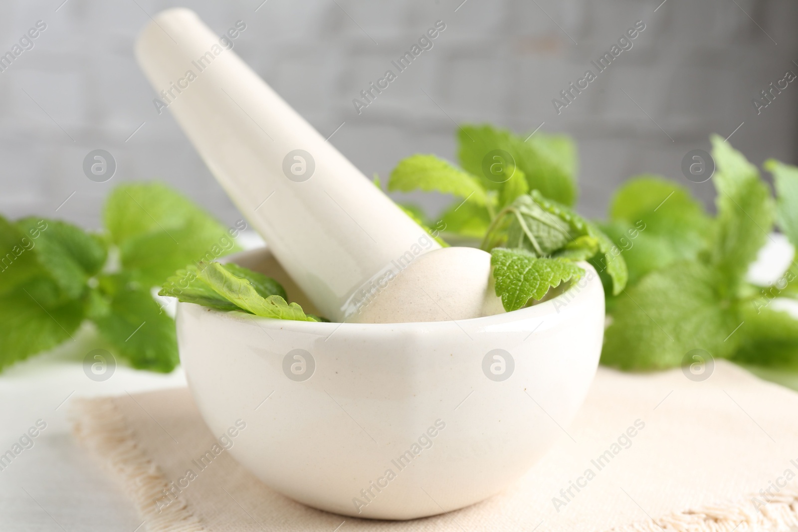 Fresh lemon balm leaves and pestle in mortar on white wooden table, closeup Photo of Fresh lemon balm leaves and pestle in mortar on white wooden table, closeup