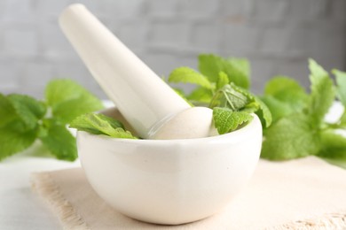 Photo of Fresh lemon balm leaves and pestle in mortar on white wooden table, closeup