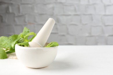 Photo of Fresh lemon balm leaves and pestle in mortar on white wooden table. Space for text