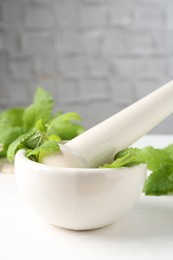 Photo of Fresh lemon balm leaves and pestle in mortar on white wooden table, closeup