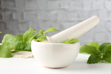 Photo of Fresh lemon balm leaves and pestle in mortar on white wooden table, closeup