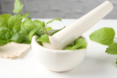 Photo of Fresh lemon balm leaves and pestle in mortar on white wooden table, closeup