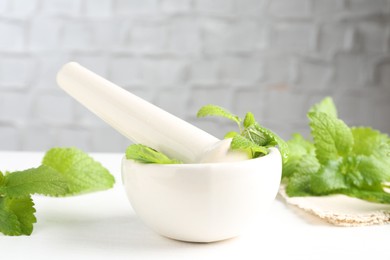 Photo of Fresh lemon balm leaves and pestle in mortar on white wooden table, closeup