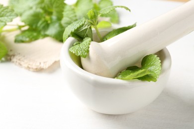 Photo of Fresh lemon balm leaves and pestle in mortar on white wooden table, closeup