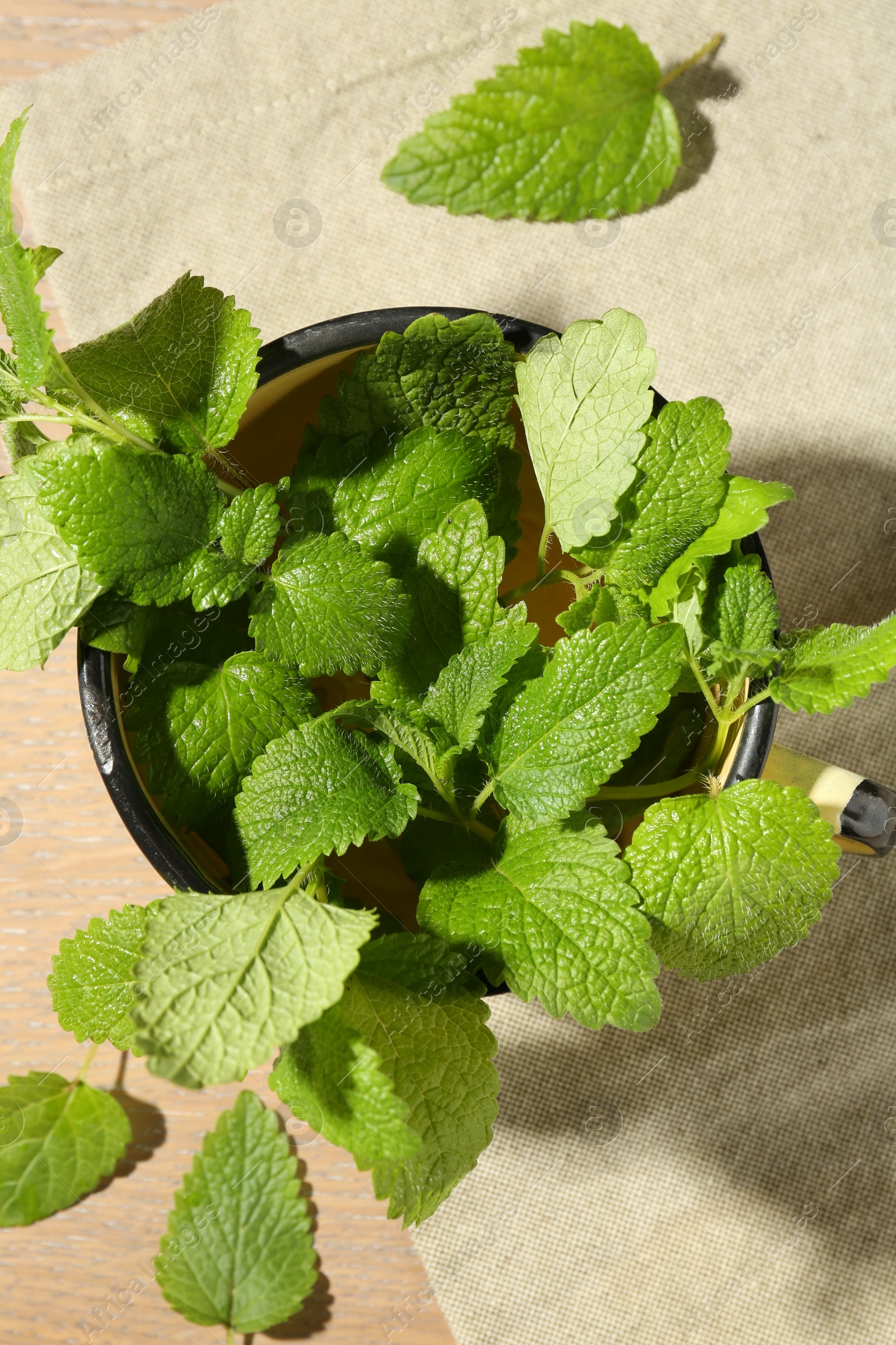 Fresh lemon balm leaves in mug on wooden table, top view Photo of Fresh lemon balm leaves in mug on wooden table, top view