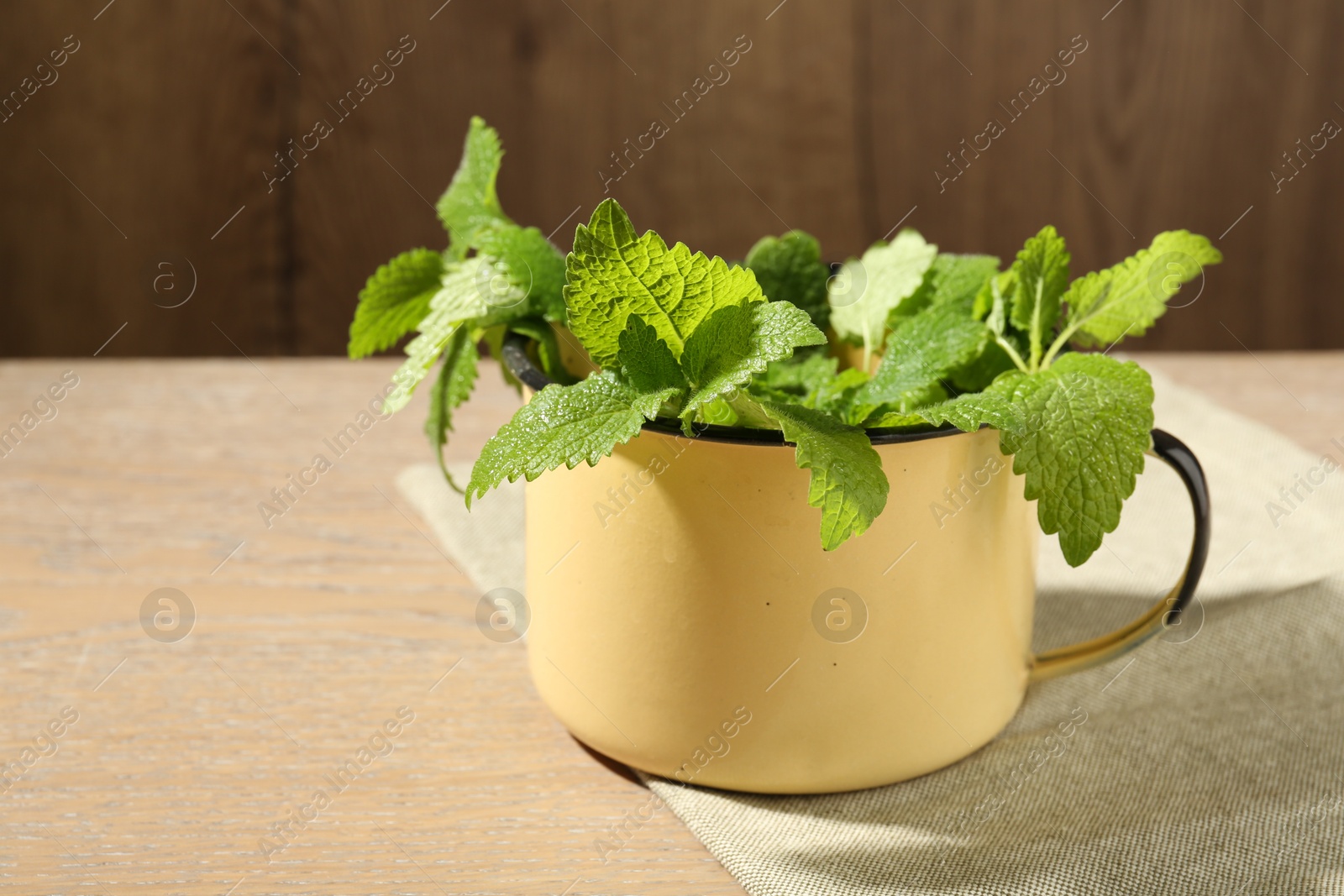 Fresh lemon balm leaves in mug on wooden table, closeup Photo of Fresh lemon balm leaves in mug on wooden table, closeup