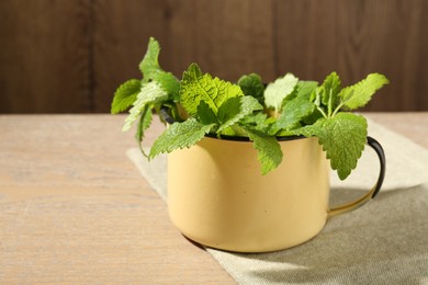 Photo of Fresh lemon balm leaves in mug on wooden table, closeup
