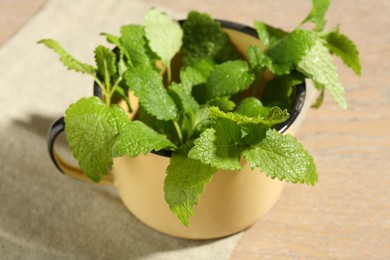 Photo of Fresh lemon balm leaves in mug on wooden table, closeup