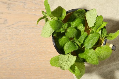 Photo of Fresh lemon balm leaves in mug on wooden table, top view. Space for text