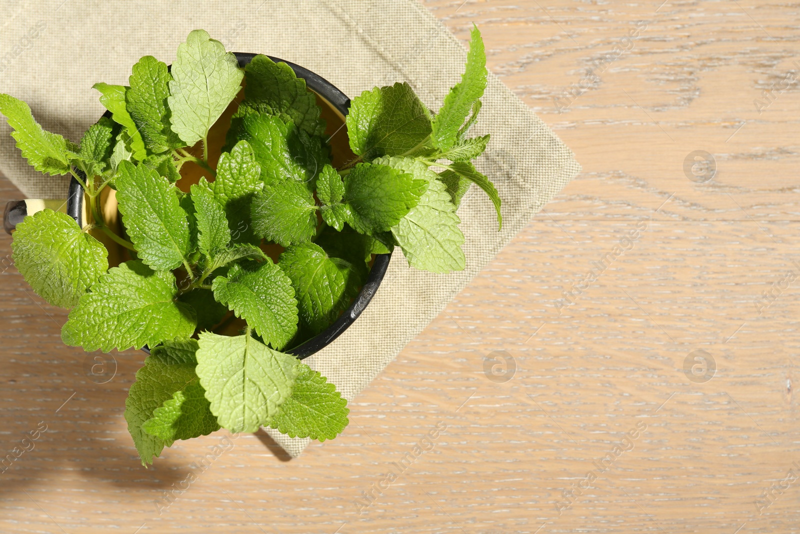 Fresh lemon balm leaves in mug on wooden table, top view. Space for text Photo of Fresh lemon balm leaves in mug on wooden table, top view. Space for text