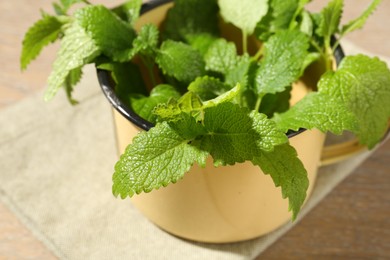Photo of Fresh lemon balm leaves in mug on wooden table, closeup