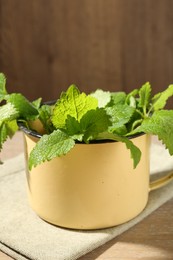 Photo of Fresh lemon balm leaves in mug on wooden table, closeup