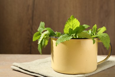 Photo of Fresh lemon balm leaves in mug on wooden table, closeup. Space for text