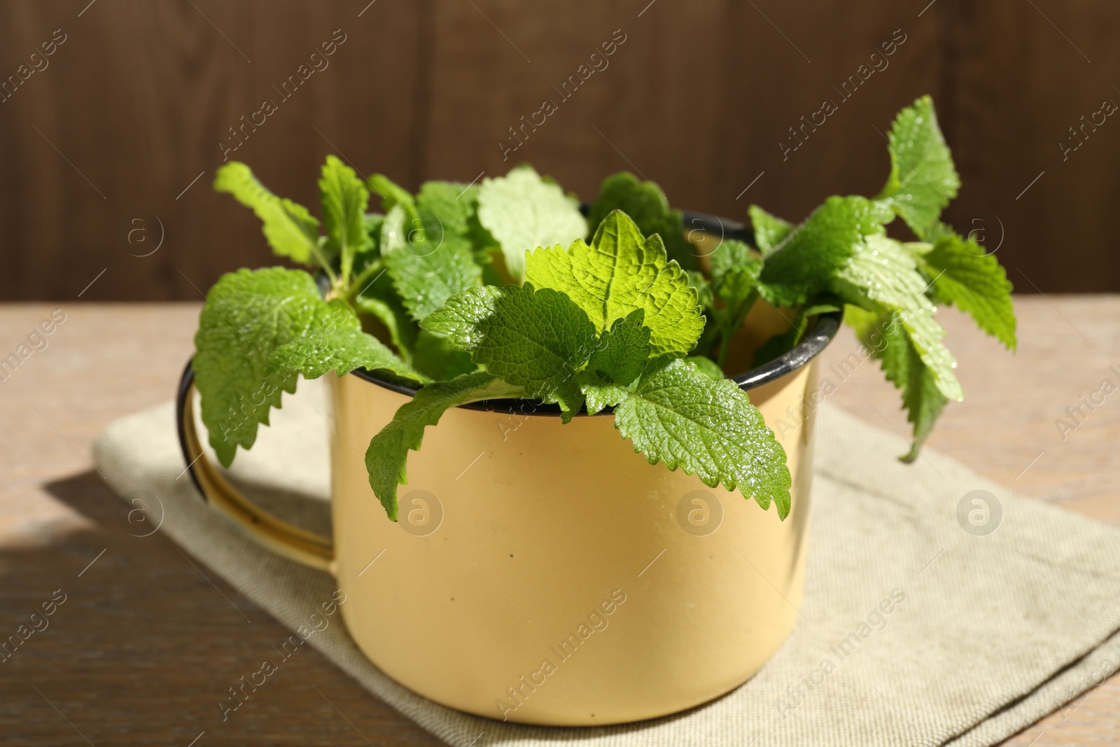 Fresh lemon balm leaves in mug on wooden table, closeup Photo of Fresh lemon balm leaves in mug on wooden table, closeup
