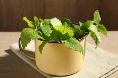 Photo of Fresh lemon balm leaves in mug on wooden table, closeup
