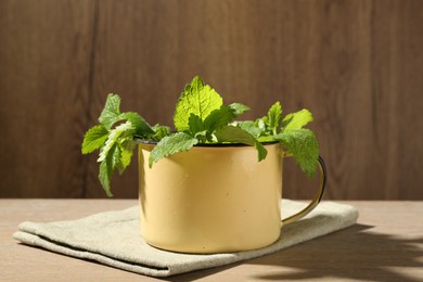 Photo of Fresh lemon balm leaves in mug on wooden table, closeup