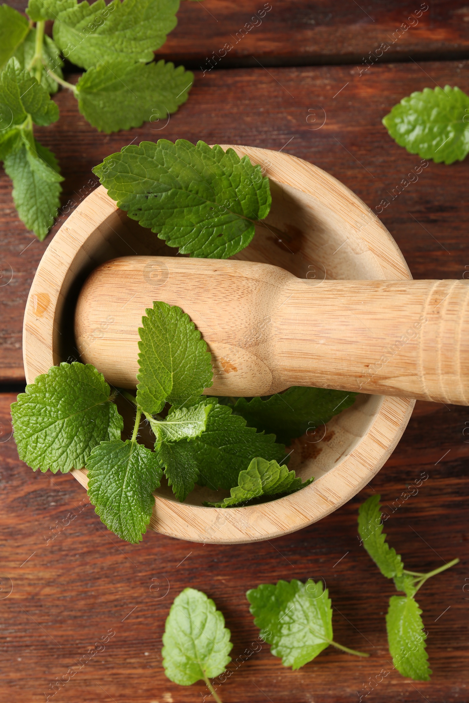 Fresh lemon balm leaves, pestle and mortar on wooden table, flat lay Photo of Fresh lemon balm leaves, pestle and mortar on wooden table, flat lay