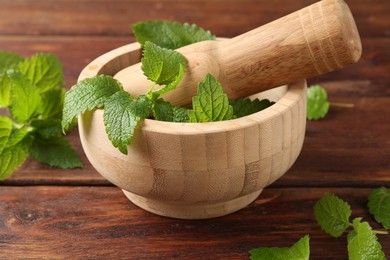 Photo of Fresh lemon balm leaves, pestle and mortar on wooden table, closeup