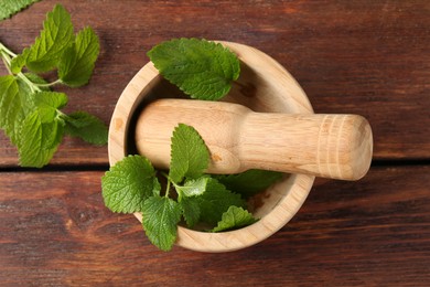 Photo of Fresh lemon balm leaves, pestle and mortar on wooden table, flat lay