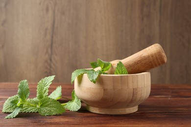 Photo of Fresh lemon balm leaves, pestle and mortar on wooden table, closeup