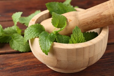 Photo of Fresh lemon balm leaves, pestle and mortar on wooden table, closeup